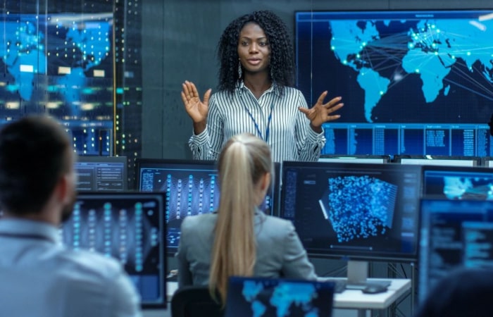 A woman standing in front of multiple monitors.